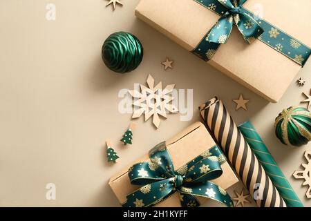 Elegant handmade gift boxes wrapped craft paper with green ribbon bow, wooden snowflakes, green balls on pastel beige background. Merry Christmas, win Stock Photo