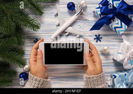 https://l450v.alamy.com/450v/2h1m1ef/traveling-as-gift-female-hands-holding-a-smartphone-for-travel-planning-christmas-background-with-model-of-plane-and-gift-boxes-mockup-2h1m1ef.jpg