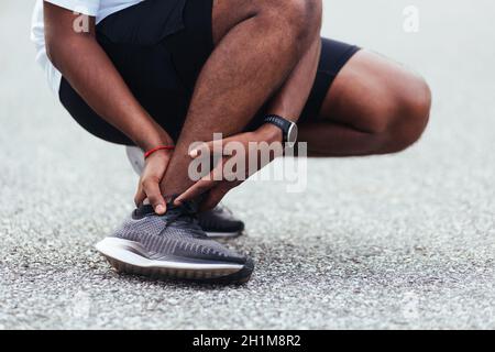 Close up Asian young sport runner black man wear watch hands joint hold leg pain because of twisted ankle broken while running at the outdoor street h Stock Photo