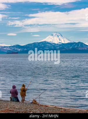 The fishermen with fishing rod on coast of Pacific ocean in the background of the volcano Stock Photo