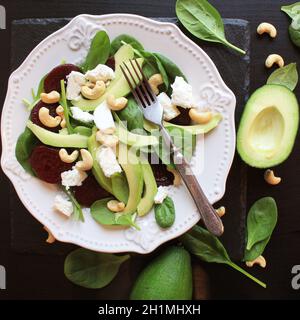 Healthy beet salad with fresh sweet baby spinach, nuts, feta cheese and avocado. Plate with salad on rustic wooden table. Top view Stock Photo