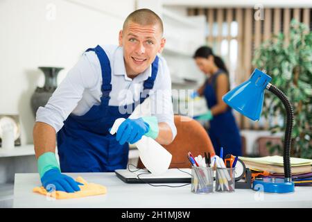 Cheerful worker of cleaning service wiping furniture in office Stock Photo