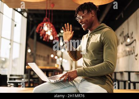 African man communicates on a laptop while sitting in the office, waving hand gesture: hello. distance learning, webinar. online virtual communication Stock Photo