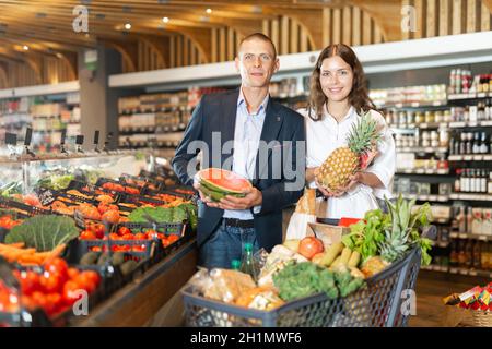 Portrait of a happy couple in a supermarket, holding a watermelon and pineapple in their hands Stock Photo