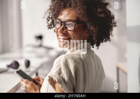 Smiling pretty lady sitting at her workplace and holding phone Stock Photo