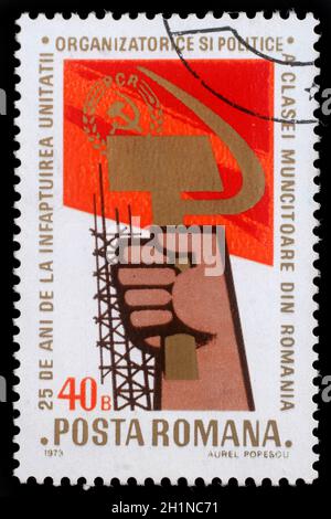 Stamp printed in Romania showing a hand holding sickle and hammer, circa 1973 Stock Photo