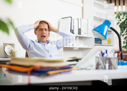 Upset office employee looking at stack of documents on table Stock Photo
