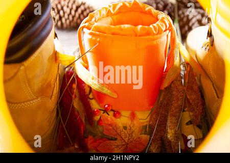 A hunter orange pouch on a wooden slab next to orange and red berries and leaves between boots with pinecones in the background Stock Photo