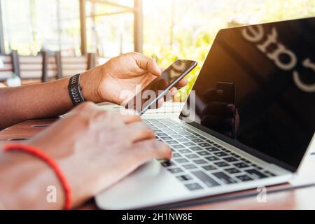 Happy Asian hand black man person working with laptop computer and reading message from modern smart phone blank screen device technology and connecti Stock Photo