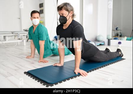 Physiotherapist assisting man in performing exercise on mat. High quality photo Stock Photo
