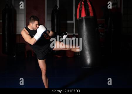 Muscular handsome kickboxing fighter giving a forceful kick during a practise round with a boxing bag. High quality photo Stock Photo