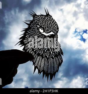 Animal figurines carved from paper in a photo of the sky. Paper-cut eagle figurine against the sky. Stock Photo