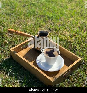 A coffee maker with a handle and a cup of coffee on a wooden tray. Stock Photo