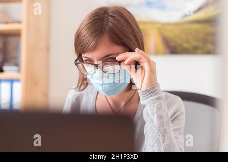 Young woman with glasses wearing face mask is working in the office during corona crisis Stock Photo
