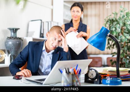 Upset office employe looking on laptop with disgruntled female manager Stock Photo