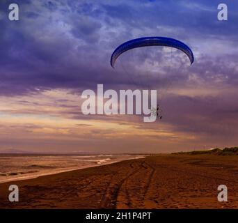 Silhouette of powered paraglider soaring flight over the sea against sunset sky Stock Photo
