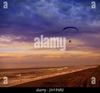 Silhouette of powered paraglider soaring flight over the sea against sunset sky Stock Photo