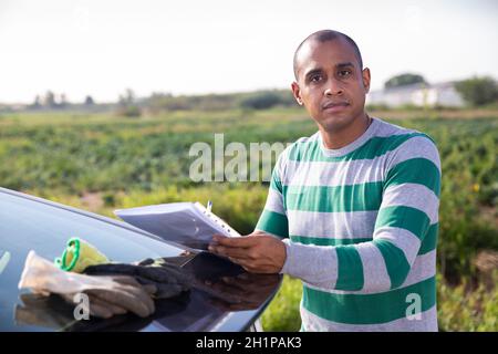 Man signing documents near car on farm Stock Photo