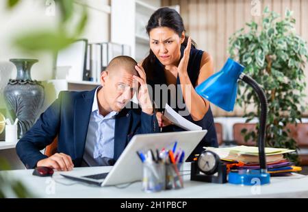 Upset office employe looking on laptop with disgruntled female manager Stock Photo