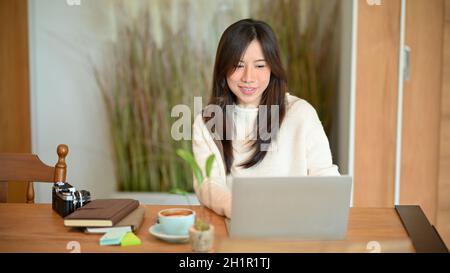 Young asian female photographer or travel blogger working on laptop computer at minimalist Japanese style coffee shop Stock Photo