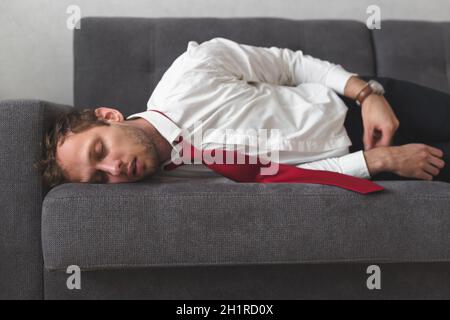 Tired overworked businessman deeply sleep on sofa. He slept all night on the couch in office clothes. Stock Photo