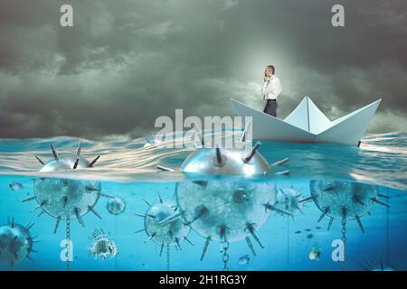 pensive businessman on a paper boat in the sea surrounded by mines. Stock Photo