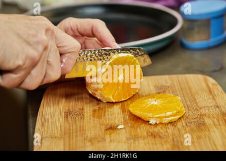 Chef cuts the orange into slices with knife. Stock Photo