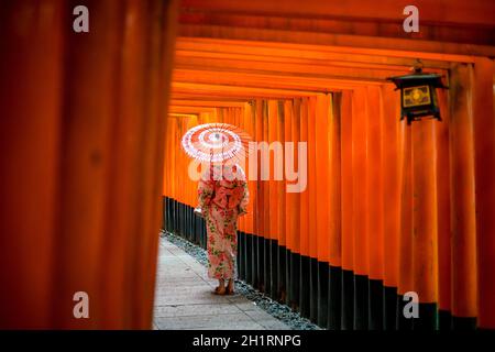 Japanese girl in Yukata with red umbrella at Fushimi Inari Shrine in Kyoto, Japan Stock Photo