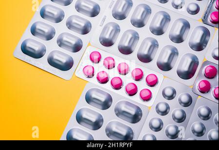 Top view round pink tablets pills in blister packs and capsule in silver aluminium foil pack on yellow background. Pharmaceutical industry. Pharmacy b Stock Photo