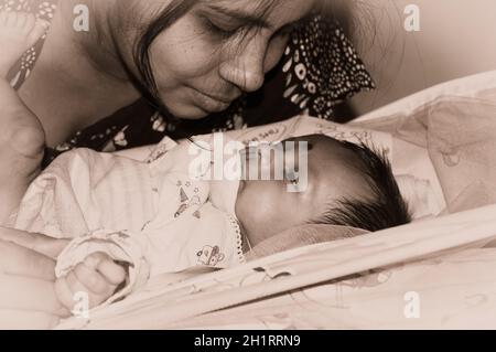 Cute newborn baby boy looks at his mother in her mother lap playing on bed. Close up. One month old Sweet little infant toddler. Indian ethnicity. Fro Stock Photo