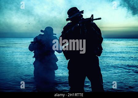 Commando soldiers walking in water, army special operations forces fighters sneaking in darkness, aiming assault rifles and observing shore during amp Stock Photo