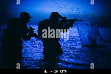 Army soldiers team, special operation forces infantrymen landing on seacoast, aiming and shooting with service rifle during firefight on shore at even Stock Photo