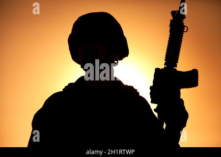 Silhouette of army soldier, special operations forces infantry rifleman, Marines fighter in combat helmet and ammunition standing with assault rifle i Stock Photo