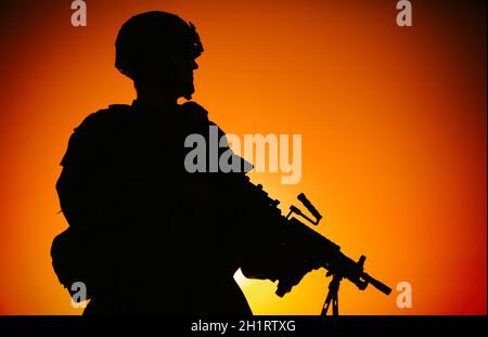 Silhouette of army infantry soldier, commando in combat helmet, armed light machine gun, standing on background of ocean horizon and sunset. Marine Co Stock Photo