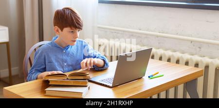 Teenager boy doing online homework at home. He is looking at the laptop. Stock Photo