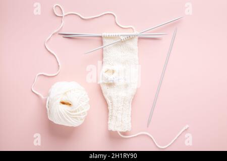 White wool knitting needles and knitted hat on pastel pink background. Female hobby knitting. Top view - Image Stock Photo