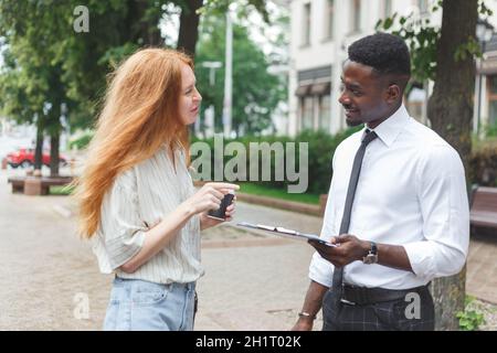 Black african american man on the street making a survey to red haired woman Stock Photo