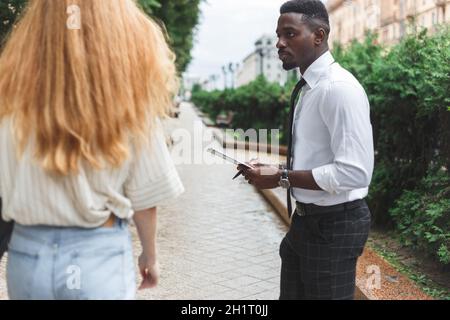 Obsessive black man in business attire interview on the street bothering passersby with questions. Stock Photo