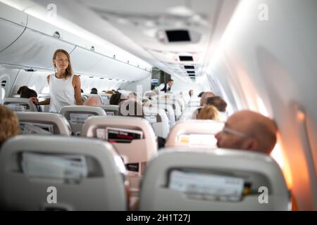 Pretty, young woman aboard an airplane during a lang haul commercial flight - stretching her legs a bit, walking in the aisle Stock Photo