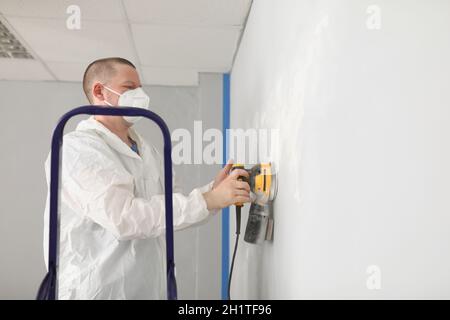 A man in uniform is grinding plaster on the wall of a house Stock Photo