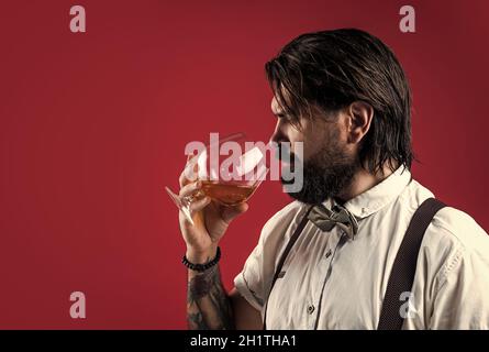 handsome hipster drinking rum glass. party goer with alcohol. brandy or cognac. bearded man in suspenders drink scotch whiskey. brutal guy bartender Stock Photo