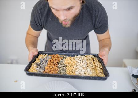 Man holding black tray of chickpeas, almonds, peanuts, pistachios, and multi-seed crispbread. Fresh crispy bread, seeds, and nuts. Healthy snacks Stock Photo