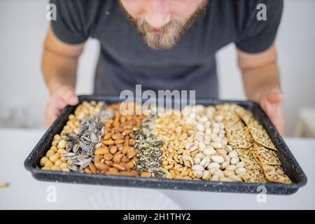 Man holding black tray of chickpeas, almonds, peanuts, pistachios, and multi-seed crispbread. Fresh crispy bread, seeds, and nuts. Healthy snacks Stock Photo