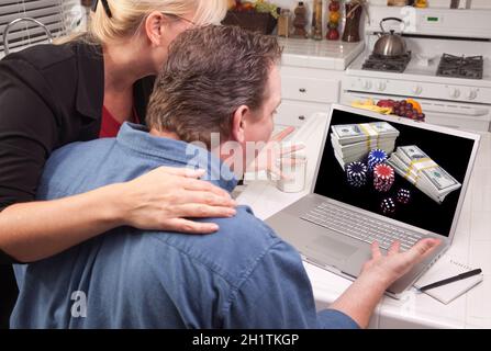 Couple In Kitchen Using Laptop with Stacks of Money and Poker Chips on the Screen. Stock Photo