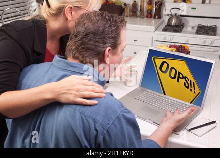 Couple In Kitchen Using Laptop with Yellow Oops Road Sign on the Screen. Stock Photo