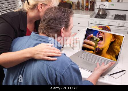 Couple In Kitchen Using Laptop with Singing Woman on the Screen. Stock Photo