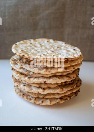 Thin round crispbreads baked with wheat, rye and barley on white and textile background Stock Photo