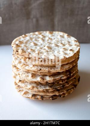 Thin round crispbreads baked with wheat, rye and barley on white and textile background Stock Photo