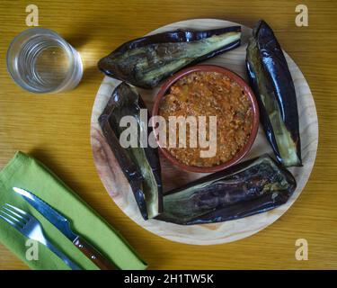 Empty Aubergine - Eggplant making a circle and  bolognesse sauce in the middle on a round wooden plate decorated decorated with cutlery on a green nap Stock Photo
