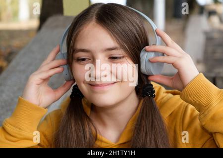 A 13-year-old girl listens to music with headphones and smiles, a large portrait. Stock Photo